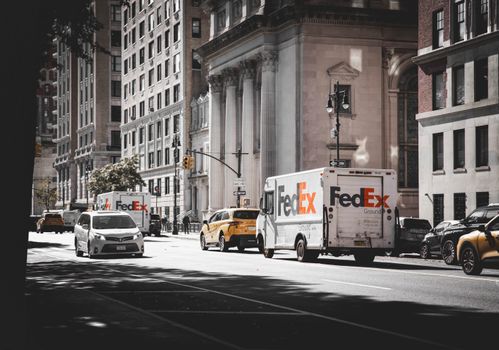 Busy street in New York City with delivery vans and cars in front of historic architecture.