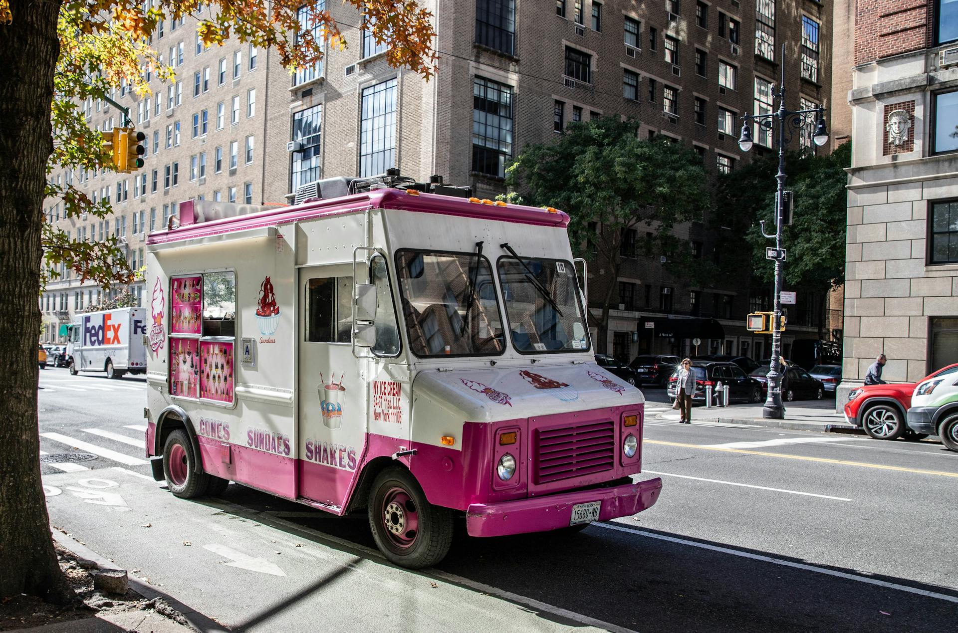 An ice cream truck parked on a sunny street in New York City, offering cones, sundaes, and shakes.