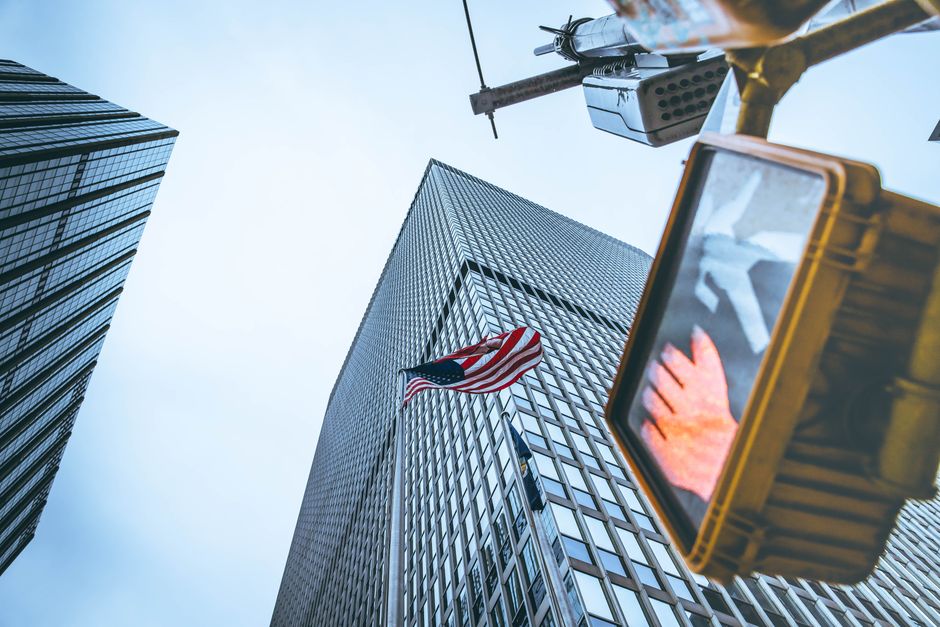 Upward view of New York City skyscrapers, American flag, and pedestrian traffic light.
