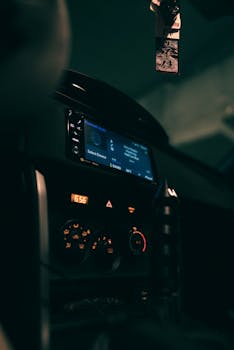 Close-up of a car dashboard with glowing controls and a hanging air freshener.