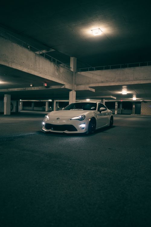 Free A sleek white sports car parked in a dimly lit parking garage, exuding a modern and moody vibe. Stock Photo