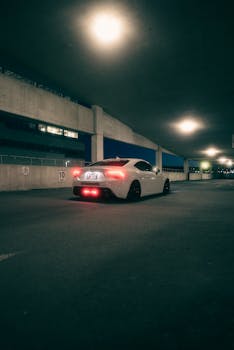 A stylish white sports car with LED lights parked under ceiling lights in an urban setting.