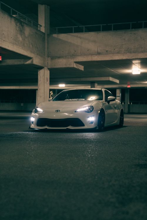 Free White sports car with headlights on in a dimly lit underground parking garage. Stock Photo