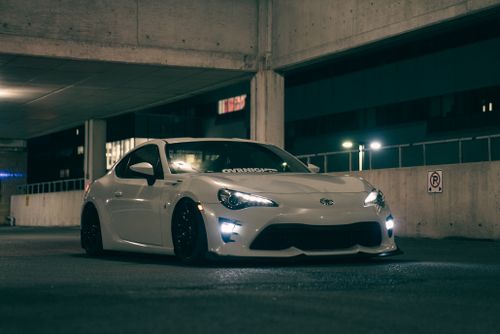 Free White sports car parked in a dimly lit urban garage, showcasing sleek design at night. Stock Photo
