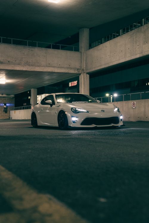 Free White sports car parked in a dimly lit urban garage at night, highlighting modern design. Stock Photo