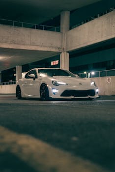 A modern white sports car parked in an urban parking garage at night, showcasing sleek design.