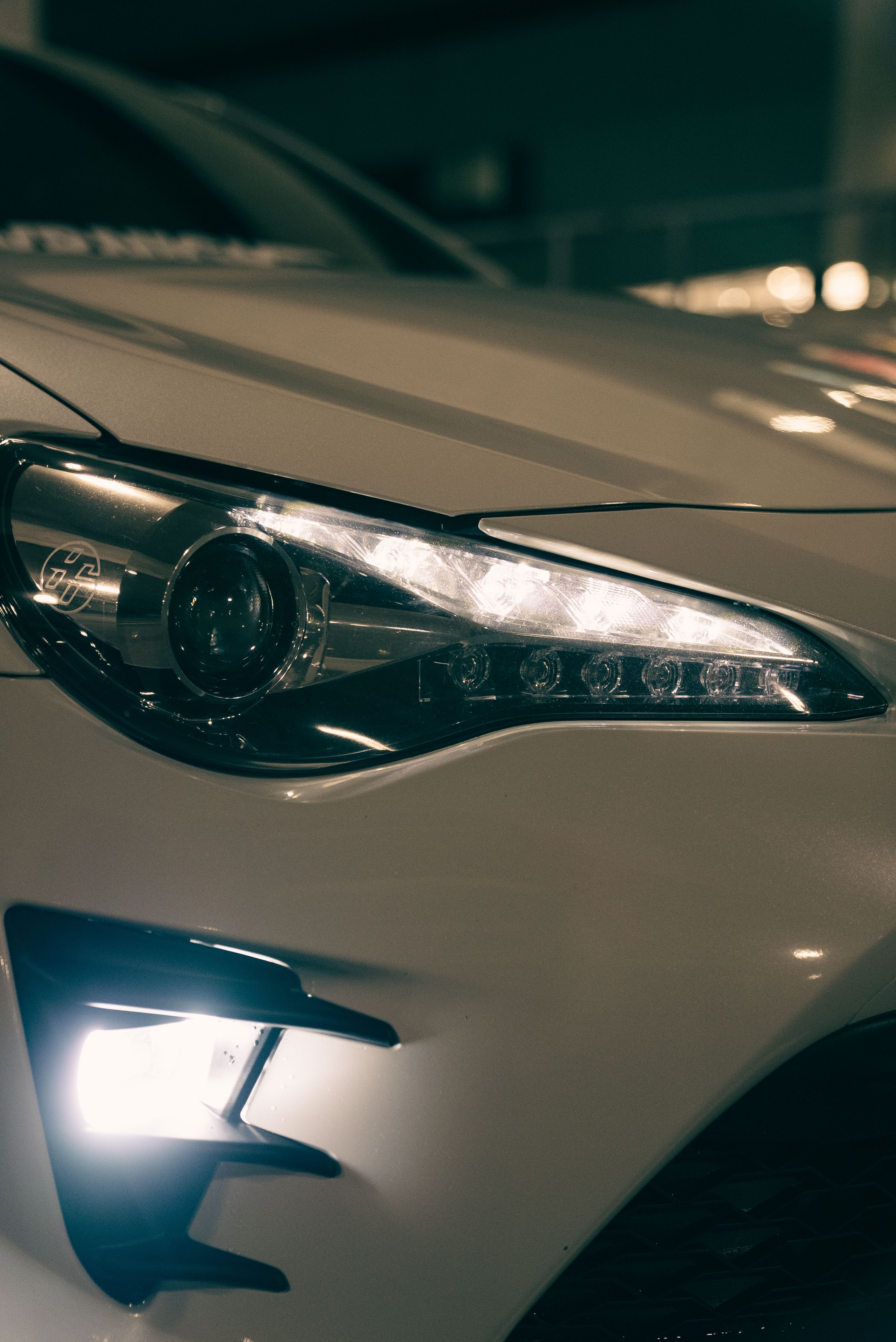 Detailed shot of a luxury sports car headlight illuminated at night, highlighting sleek design.