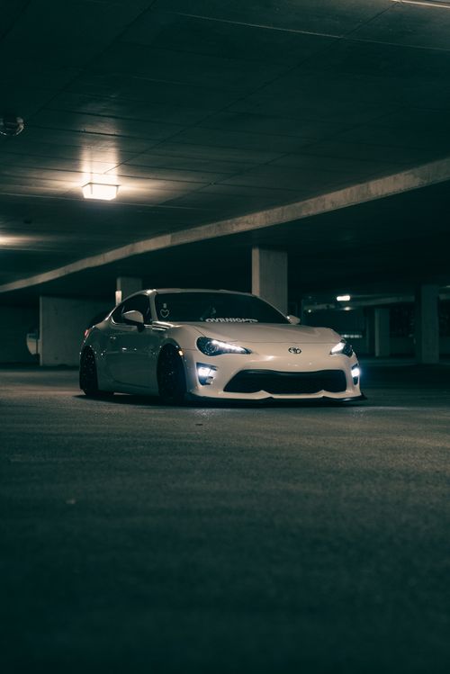 Free White sports car parked in a dimly lit underground garage, exuding a cool and modern vibe. Stock Photo