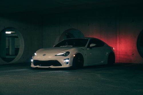 Free A sleek white sports car parked in a dimly lit underground garage with a red glow. Stock Photo