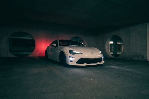 Free A white sports car parked stylishly in a dimly lit urban garage setting. Stock Photo