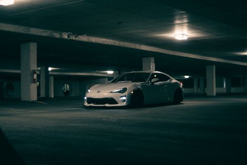 Free White sports car parked in dim, empty underground garage with atmospheric lighting. Stock Photo
