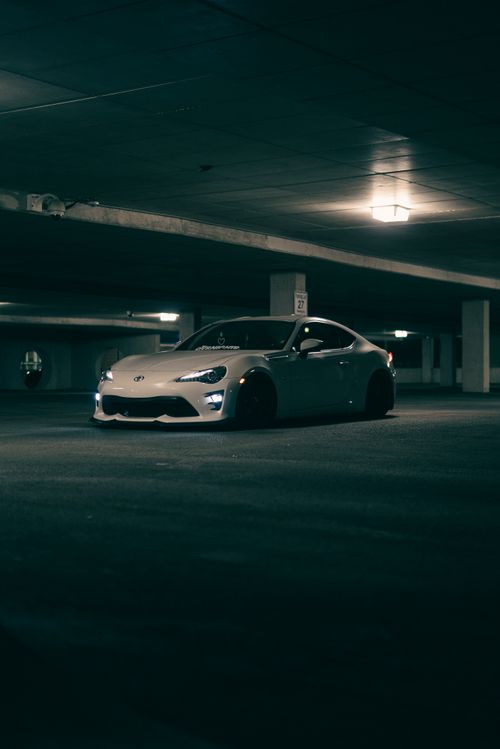 Free White sports car parked in a dimly lit underground garage, emphasizing urban solitude. Stock Photo