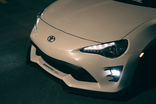 A detailed view of a white sports car parked in a dimly lit area, showcasing its headlights and sleek design.