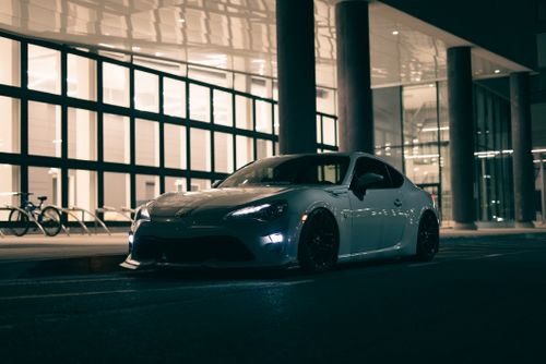 Free Modern sports car parked in front of a brightly lit urban building at night, exuding elegance and speed. Stock Photo