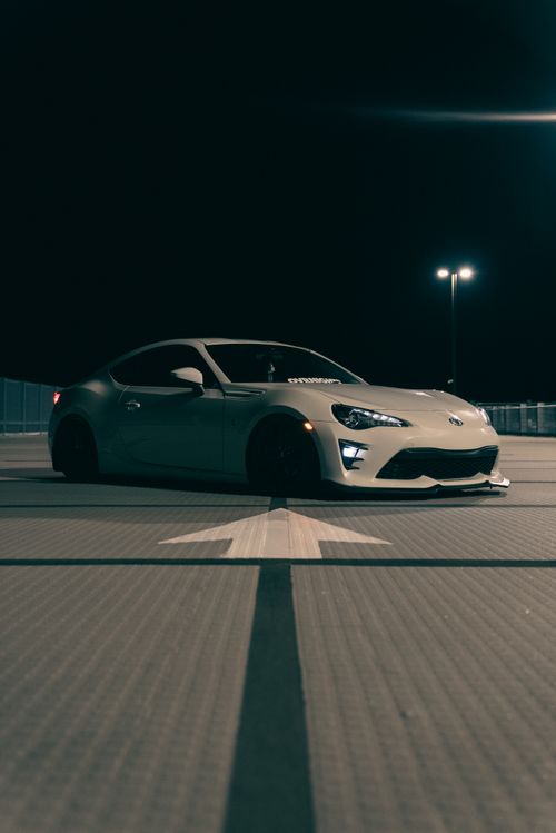 Free A sleek sports car parked in a dimly lit empty lot at night with directional arrow. Stock Photo