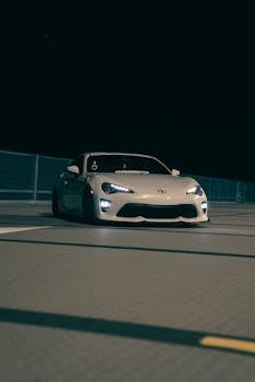 Stylish sports car with headlights on parked on urban street at night, exuding a cool and modern vibe.