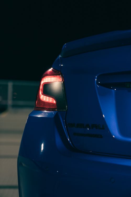 Free Detailed view of a blue car's tail light illuminated in a dimly lit parking area. Stock Photo