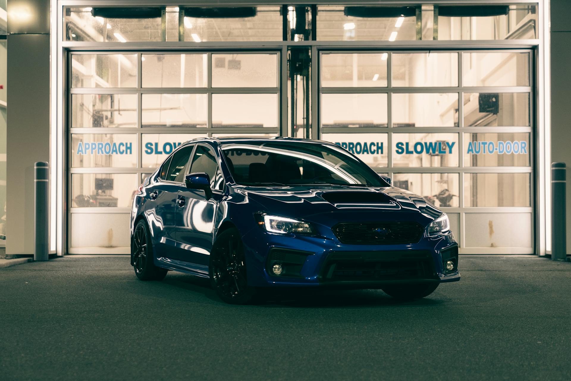 A blue car is parked in front of a garage door at night, showcasing its sleek design.