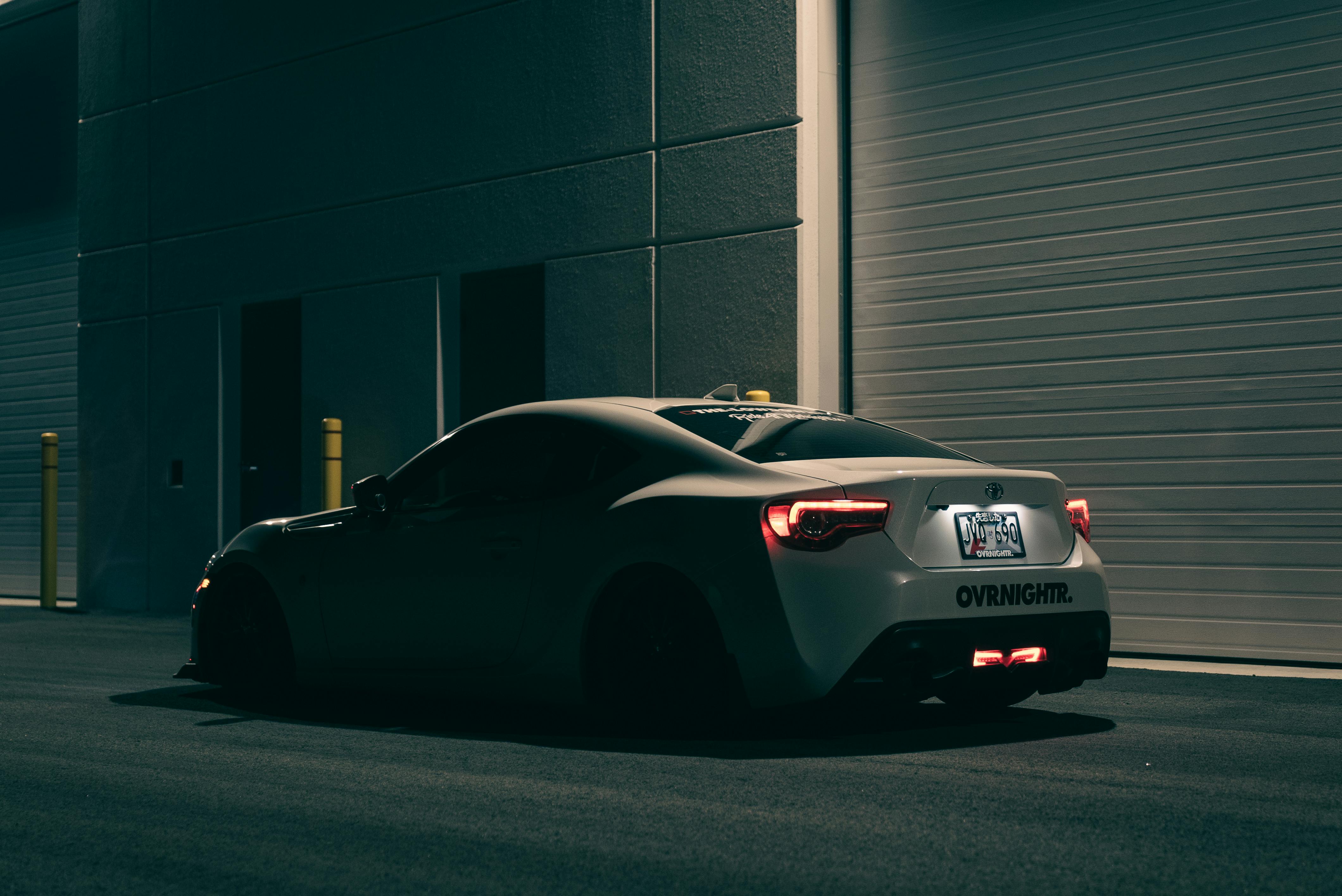Free A sleek modern sports car parked at night beside a building, showcasing urban style. Stock Photo
