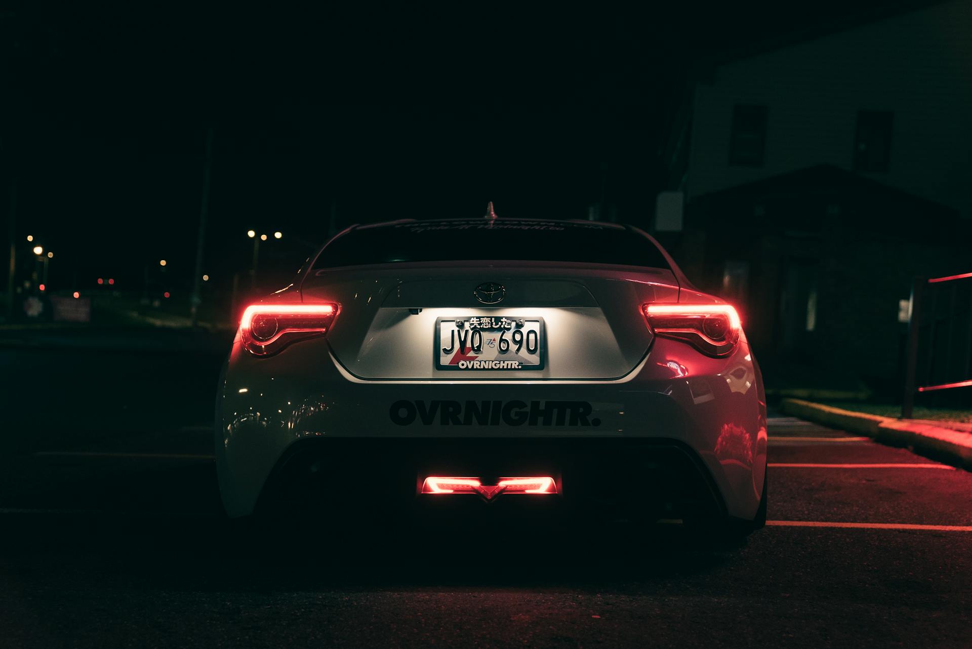 A sleek car is captured in the night, showcasing its bright tail lights and rear license plate.