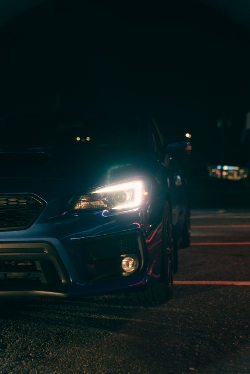Free Front view of a blue car with headlights on at night in a parking lot. Stock Photo