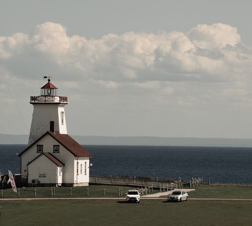 Free Picturesque lighthouse by the ocean with cars parked nearby under a cloudy sky. Stock Photo