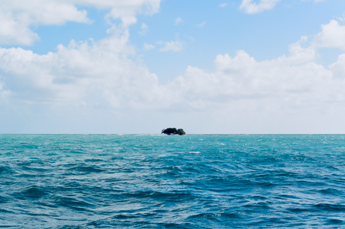 Free Vibrant blue ocean and isolated tropical island under a bright sky. Stock Photo