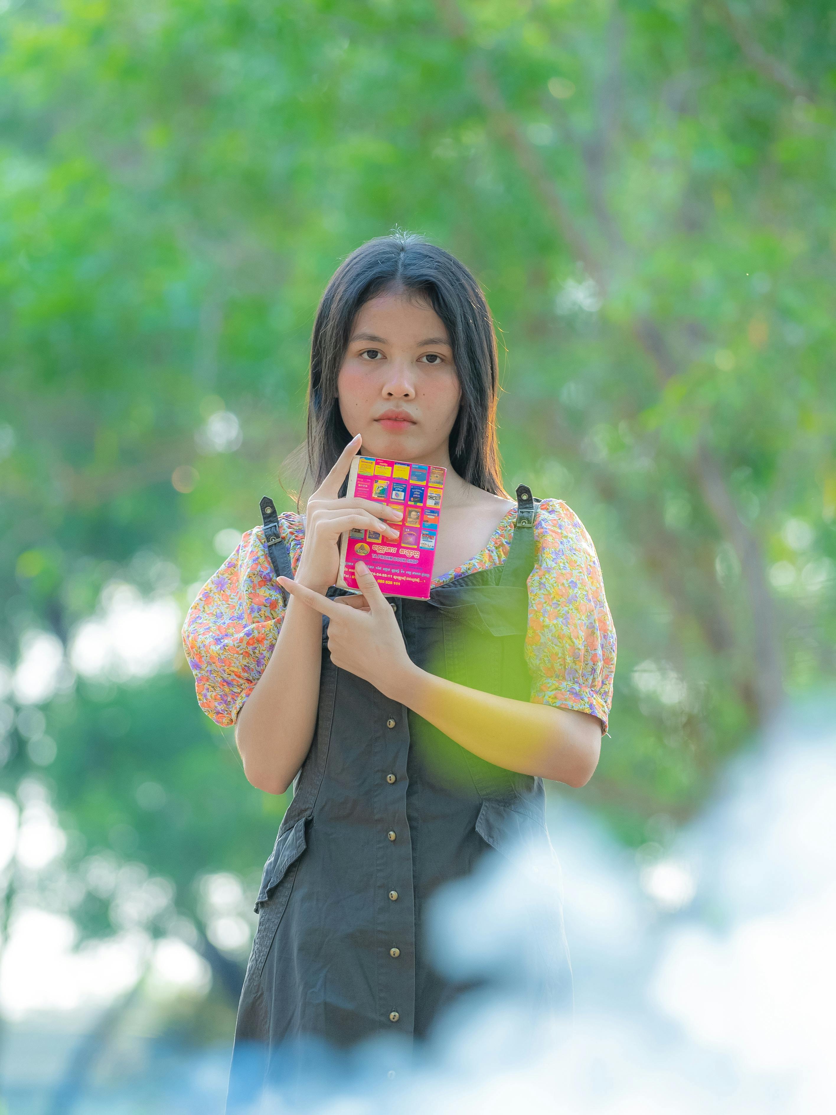 ingyenes Portré egy fiatal nőről, aki színes cukorkát tart buja zöld háttér előtt, elgondolkodtató pózban. Stockfotó