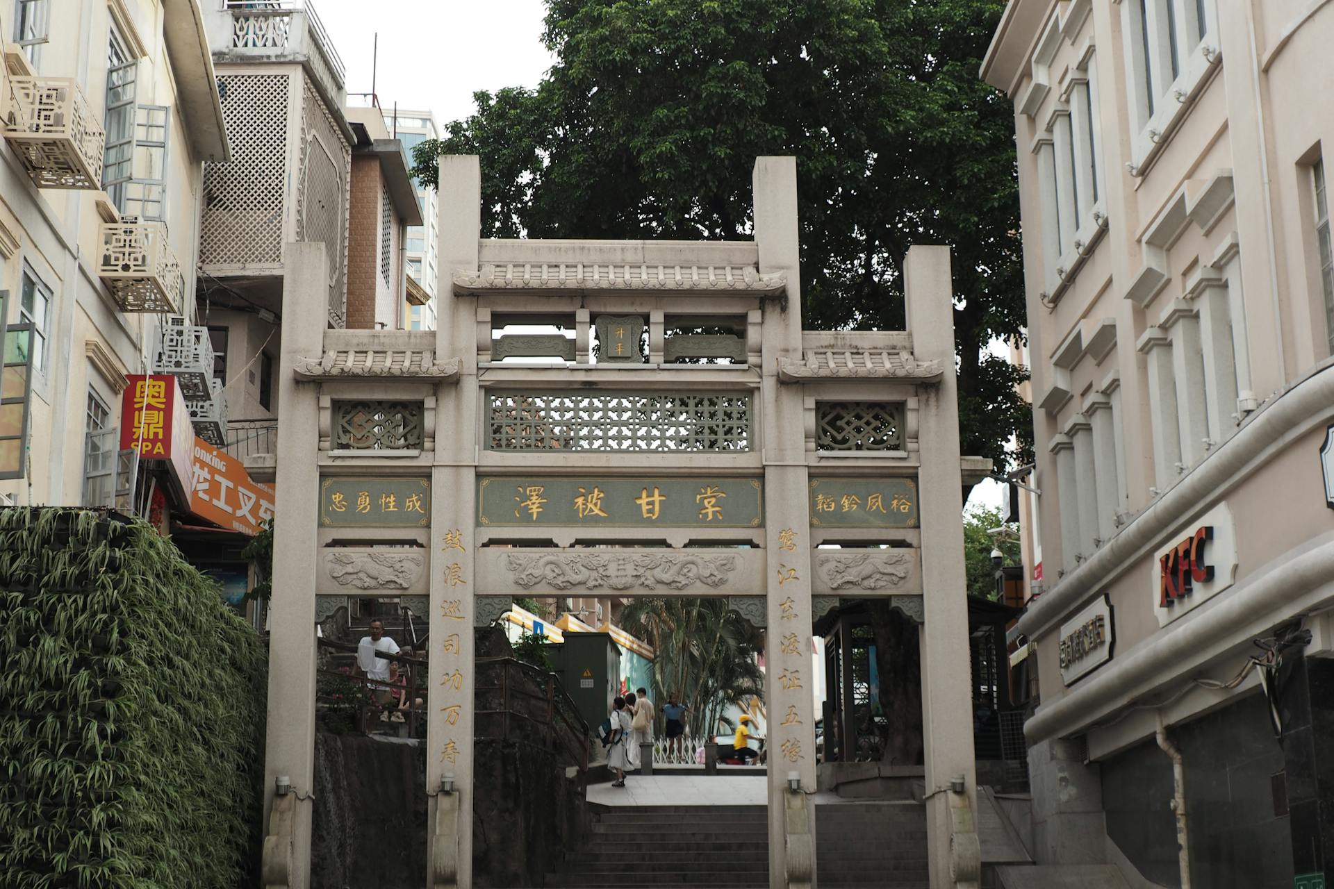 A traditional stone gateway amidst city architecture, with signs and a KFC building nearby.