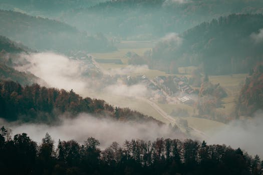 Aerial view of a misty mountain valley with autumn trees and a small village.