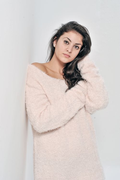 Free A woman with dark hair in a fluffy sweater poses against a white wall. Stock Photo