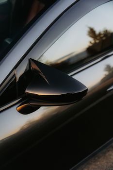 Close-up of a black car side mirror reflecting a sunset scene, emphasizing sleek design and style.