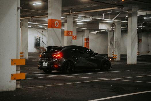 A modern black car parked in a dimly lit underground parking garage, creating a moody urban atmosphere.