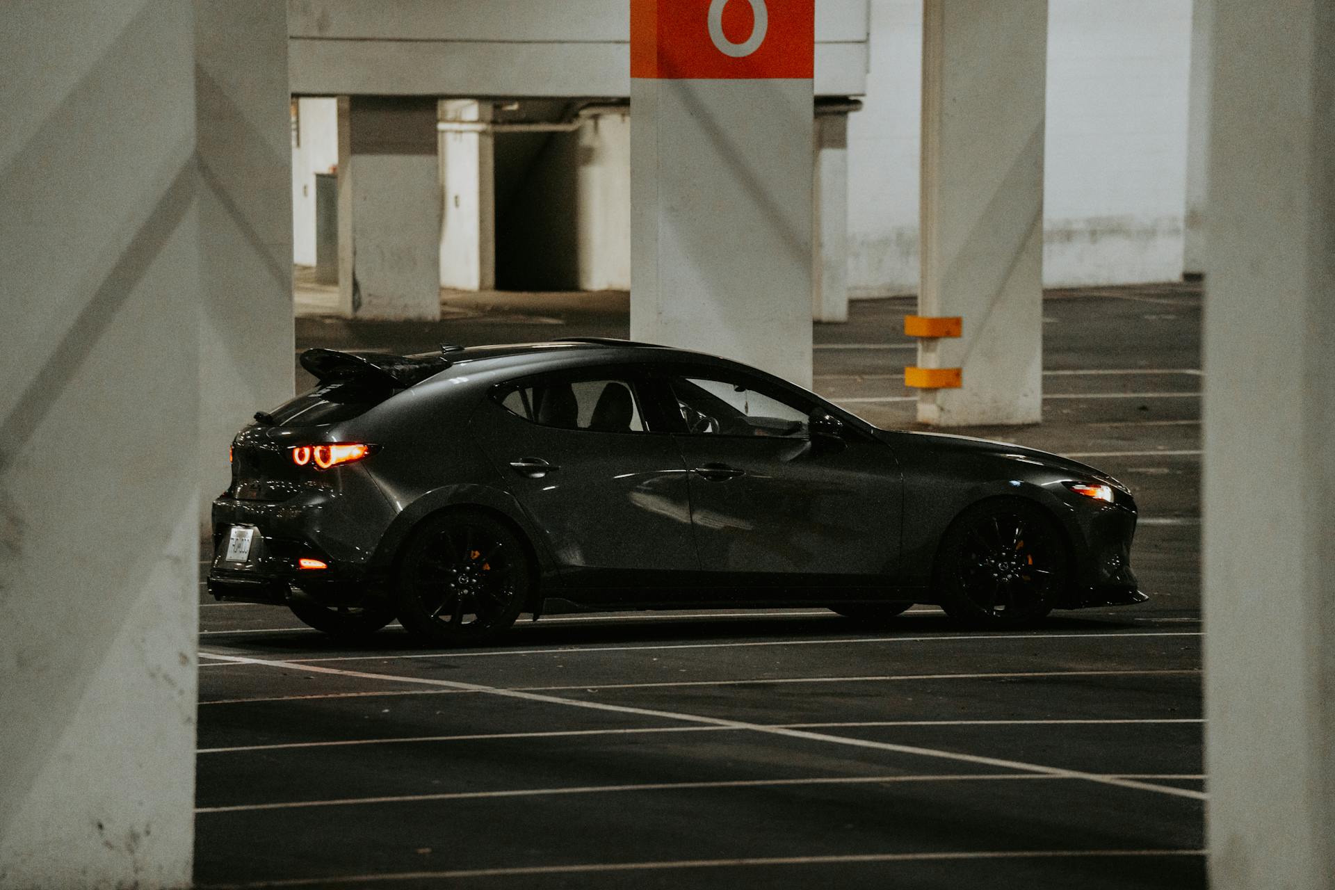 A modern car parked in an underground parking garage with industrial lighting and concrete pillars.