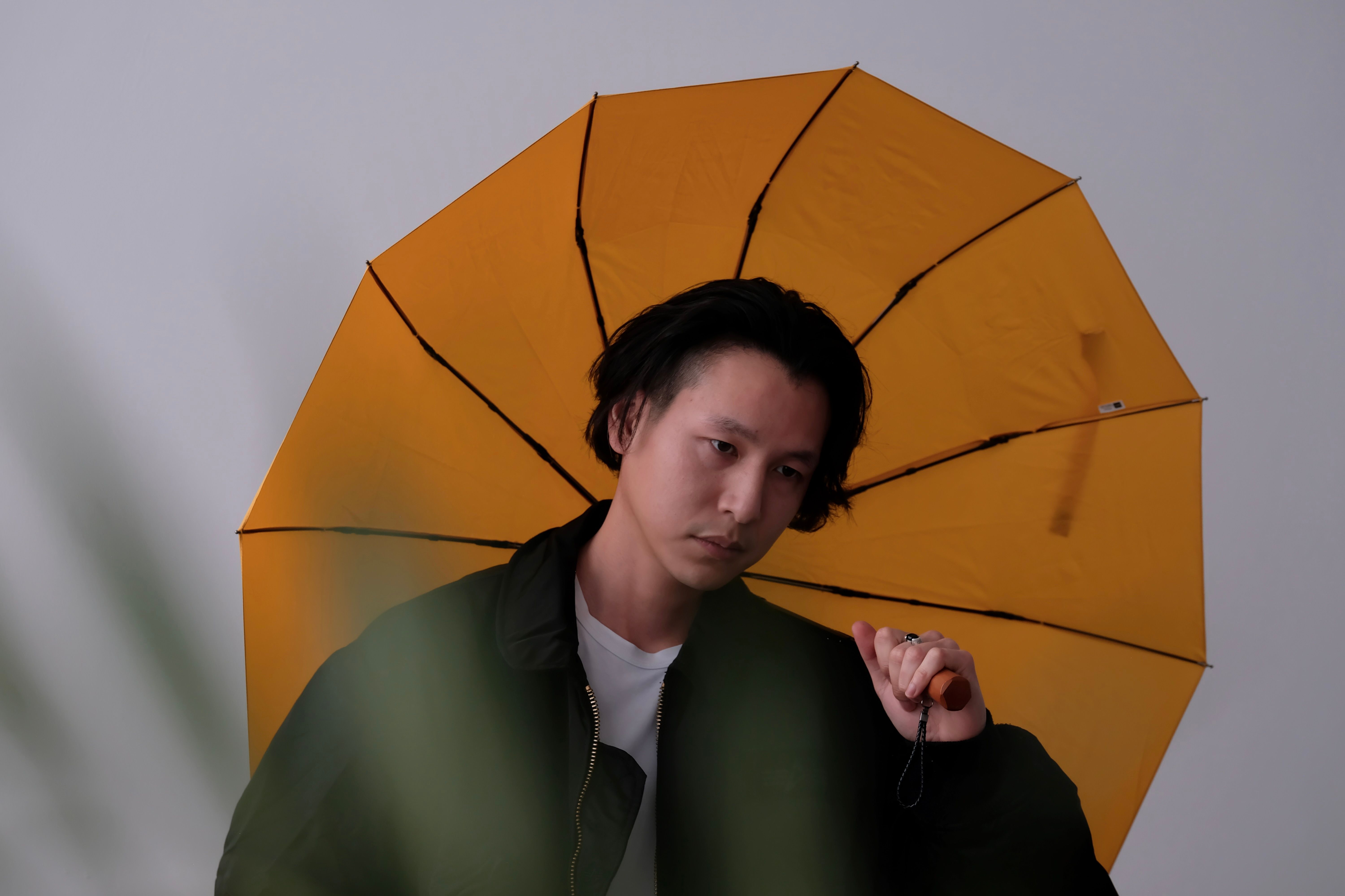 Portrait of an Asian man posing with a vibrant yellow umbrella in a studio setting.