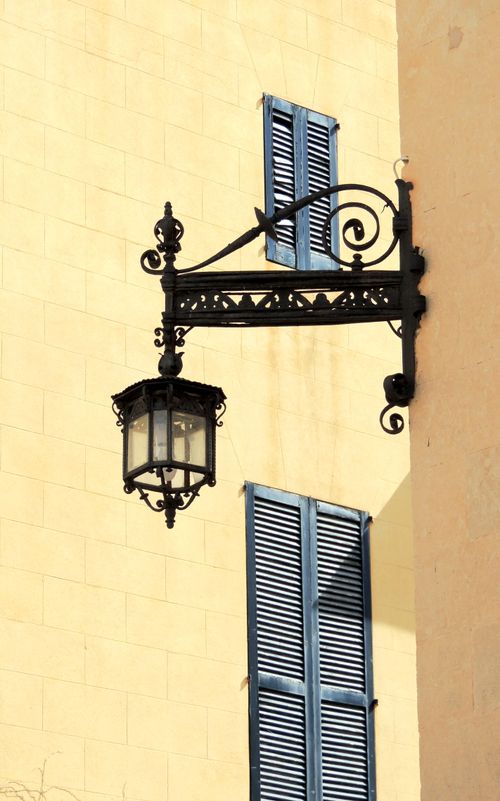 Free A classic black lantern on Alcúdia's wall alongside blue shuttered windows, Balearic Islands. Stock Photo