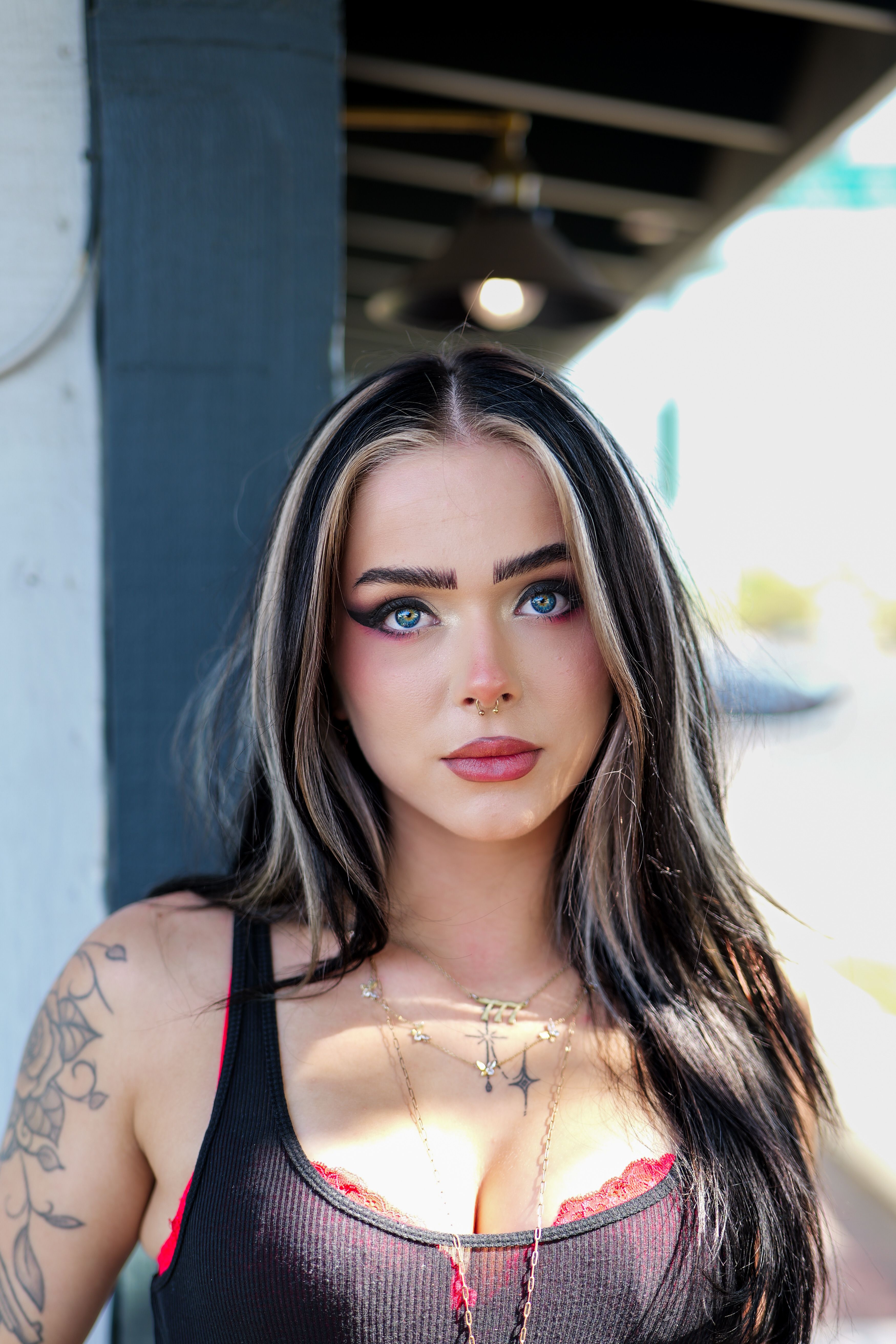 Portrait of a young woman with striking makeup and tattoos in an outdoor setting.