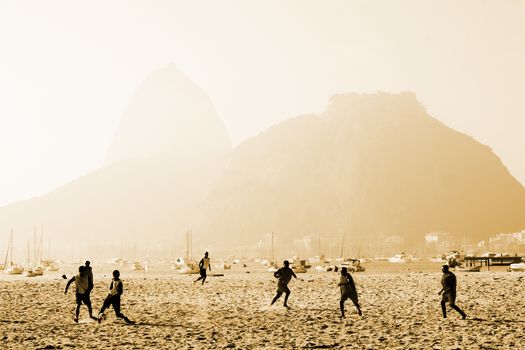 Dynamic beach soccer game with Sugarloaf Mountain in Rio de Janeiro.