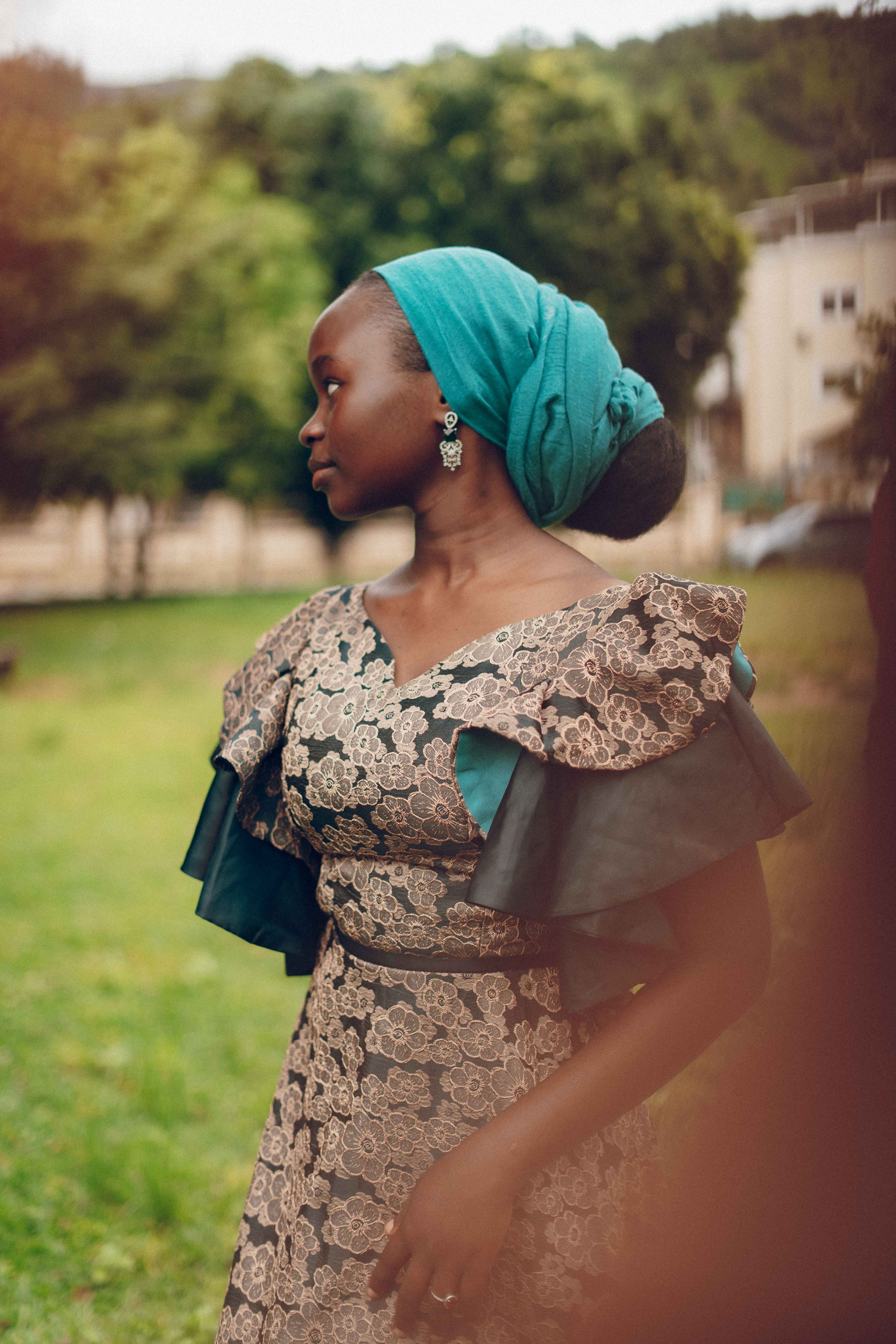 Portrait of a beautiful African woman in traditional lace dress with headwrap, standing outdoors.