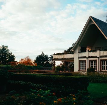 A charming suburban house surrounded by lush greenery and autumn foliage on a cloudy day.