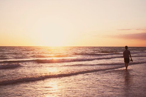 Free A person walking barefoot on a serene beach during sunset in Florida, USA. Stock Photo