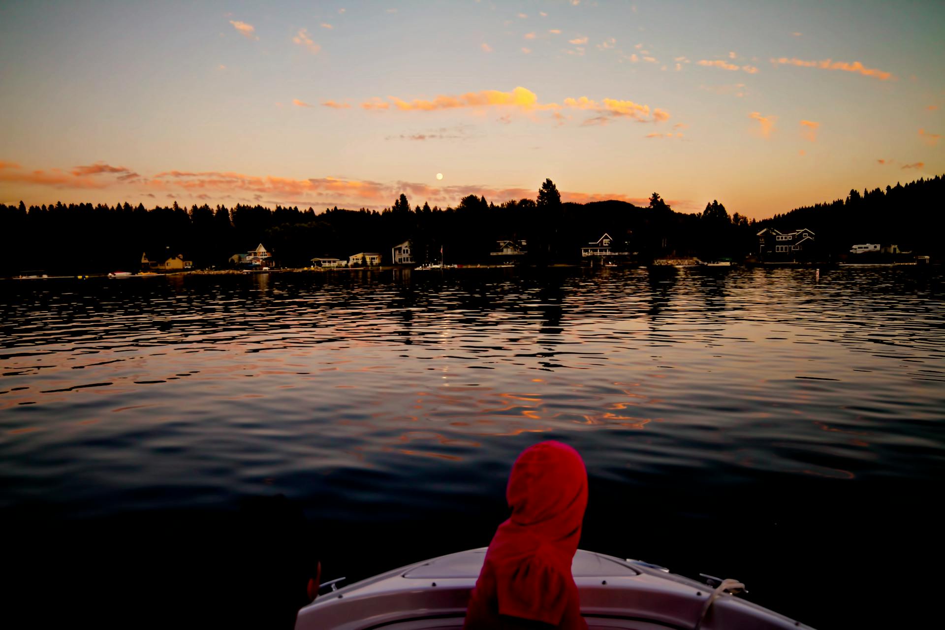 A peaceful sunset boat ride on a calm lake with silhouette of trees and houses.