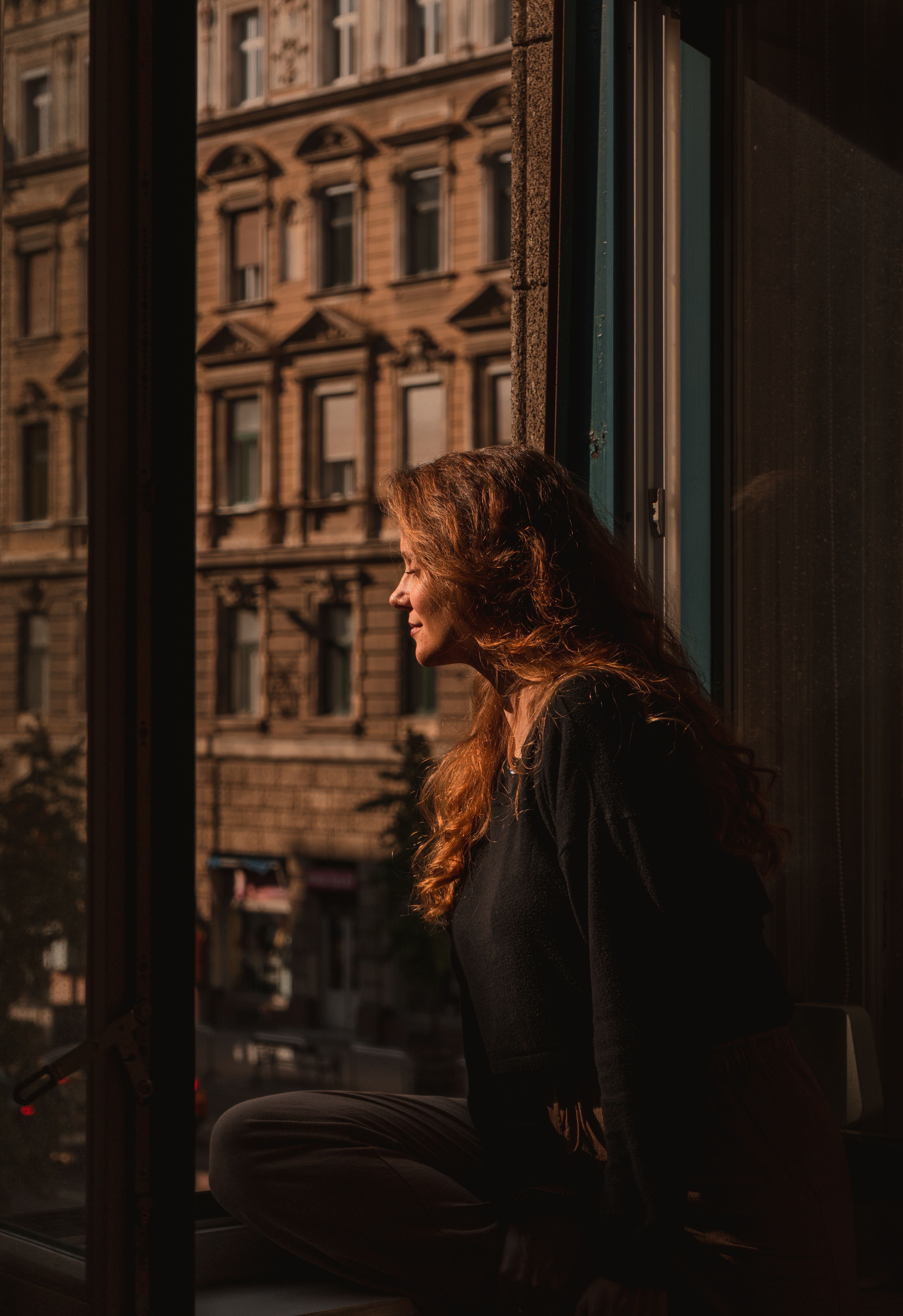 Profile portrait of a woman gazing out a window with Budapest's historic architecture in the background.