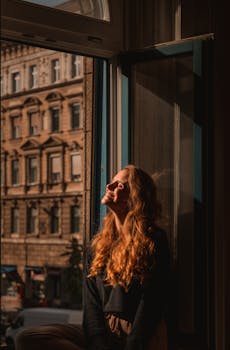 Warm portrait of a woman enjoying sunlight by a window in Budapest.