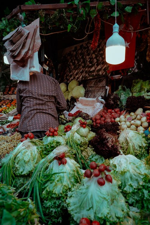 Free Vibrant market stall overflowing with fresh vegetables and leafy greens under warm lighting. Stock Photo