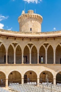Elegant arches in Bellver Castle courtyard, Palma, Spain under a bright blue sky.