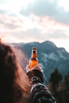 日落时分，一个人拿着啤酒瓶，欣赏山景，捕捉到茶点的时刻