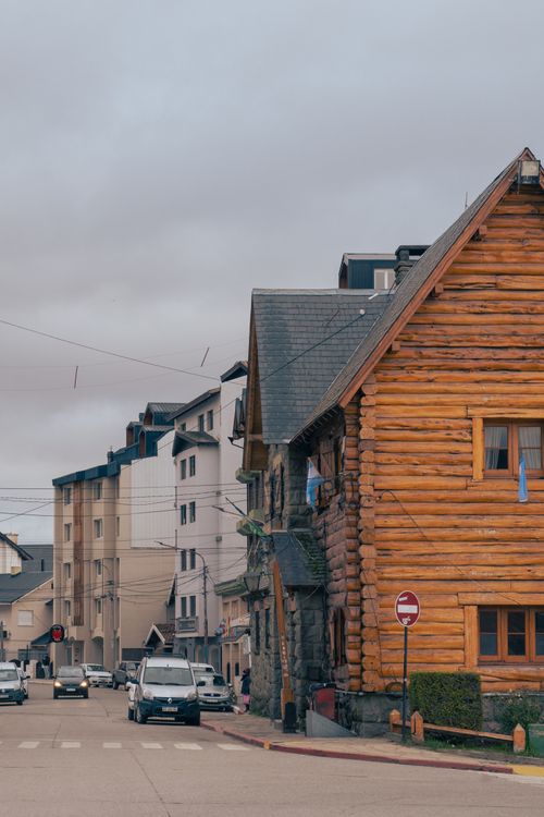 Free A charming log cabin stands at a street corner beside urban buildings under overcast skies. Stock Photo