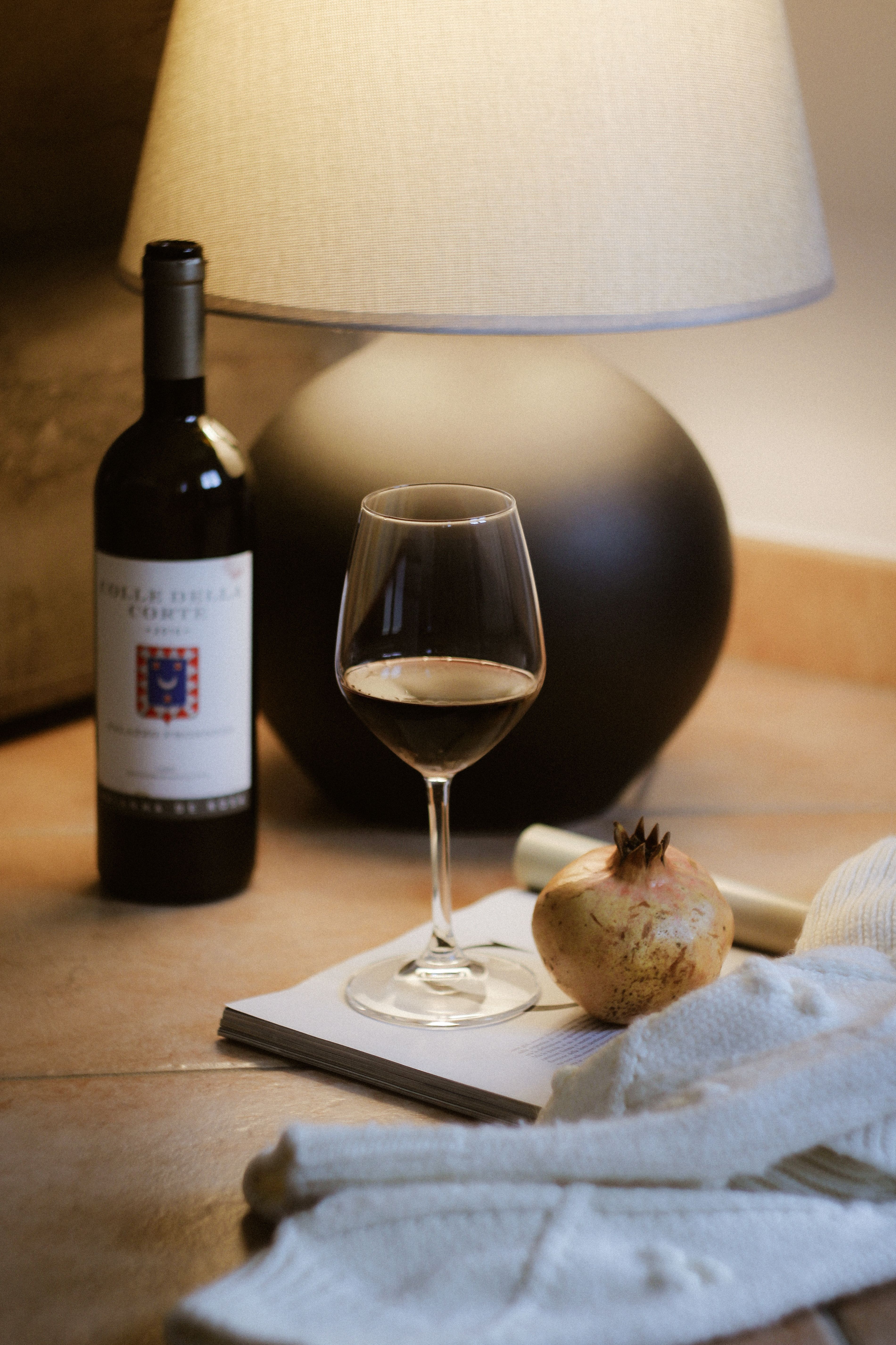 A cozy scene featuring wine, a lamp, and a pomegranate on a table.