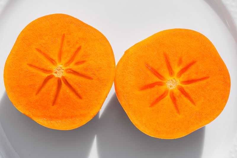 Persimmon: Top Health Benefits Of This Fall Superfruit Bright orange persimmon slices showcasing texture and freshness on a white plate